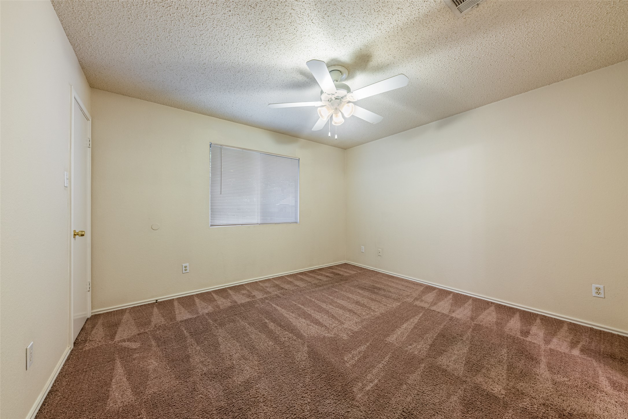 7216 Aldea Drive, Unit A Austin, TX 78745 - Photo 21 of 25 Spacious interior room with neutral-toned walls, patterned carpet flooring, a window with blinds, a ceiling fan with integrated lighting, and a white interior door with a brass-finish knob