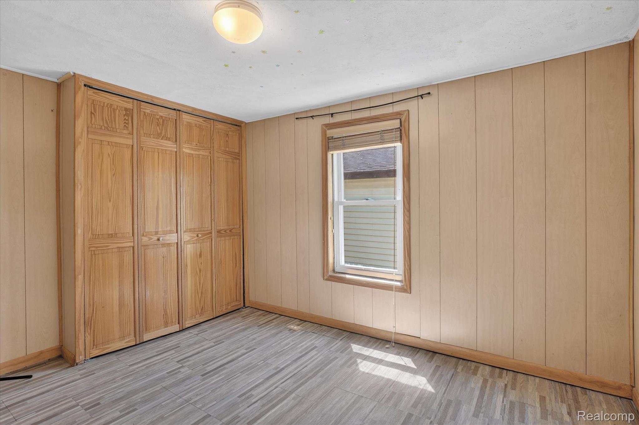 508 Deland Road Flushing, MI 48433 - Photo 22 of 38 Room featuring wood-finish flooring, light-toned vertical paneled walls, a single window with wood trim, and a full-wall built-in wardrobe with bifold doors