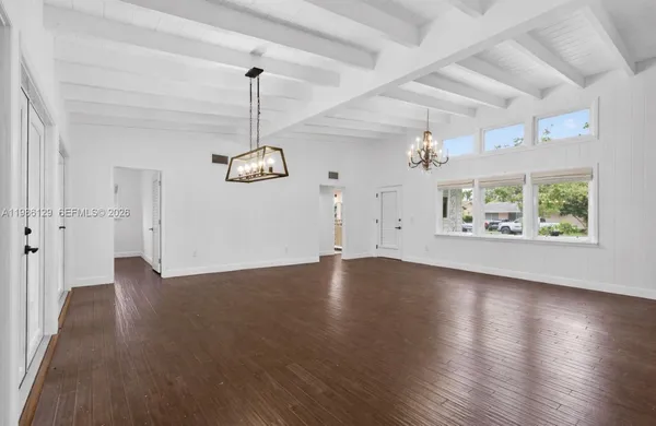 an empty room with wooden floor chandelier and windows