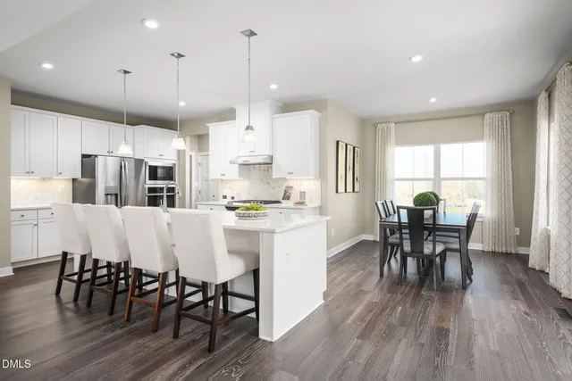 a kitchen with stainless steel appliances granite countertop a dining table chairs stove a sink and white cabinets