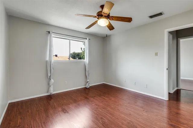 an empty room with wooden floor fan and windows
