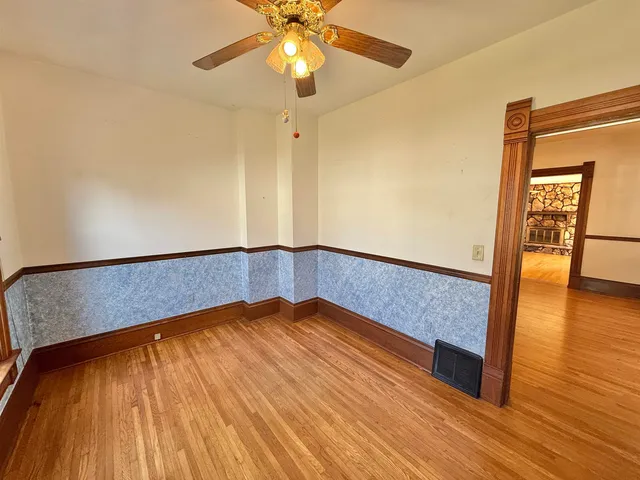 a view of an empty room with wooden floor and a ceiling fan
