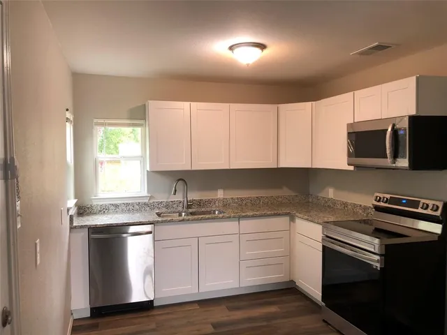 a kitchen with granite countertop white cabinets stainless steel appliances a sink and a window
