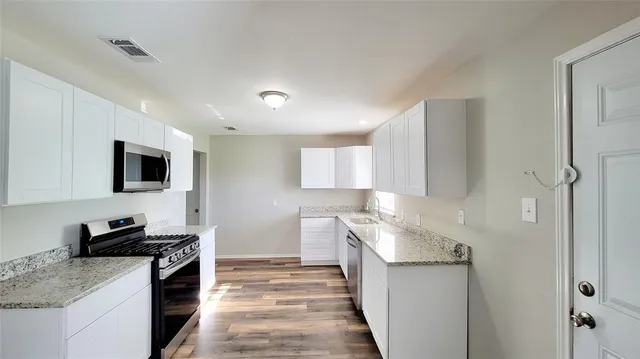 a kitchen with stainless steel appliances a stove top oven a sink a refrigerator white cabinets and wooden floor