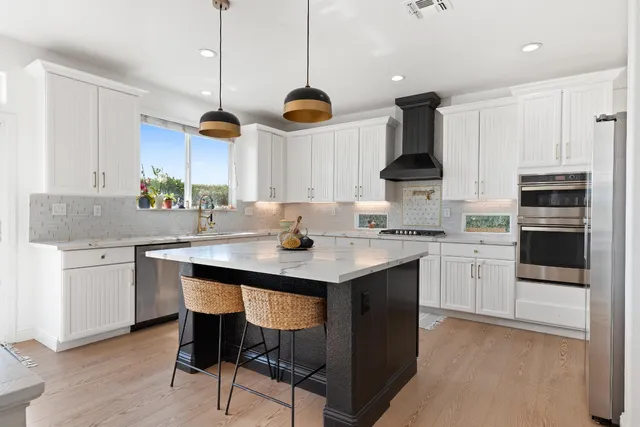 a kitchen with stainless steel appliances granite countertop a sink a stove a refrigerator and island with wooden floor