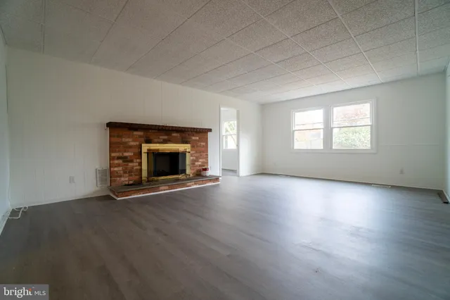 an empty room with wooden floor fireplace and windows