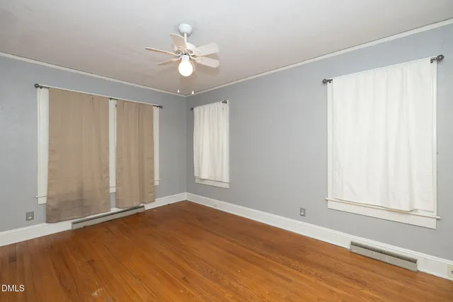 an empty room with wooden floor fan and windows