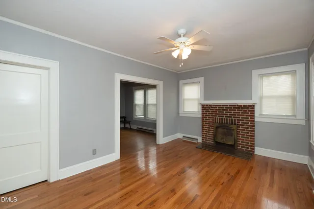 an empty room with wooden floor fireplace and windows