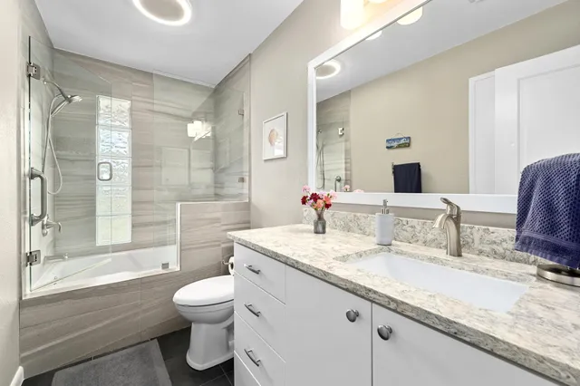 a bathroom with a granite countertop sink mirror vanity bathtub and toilet
