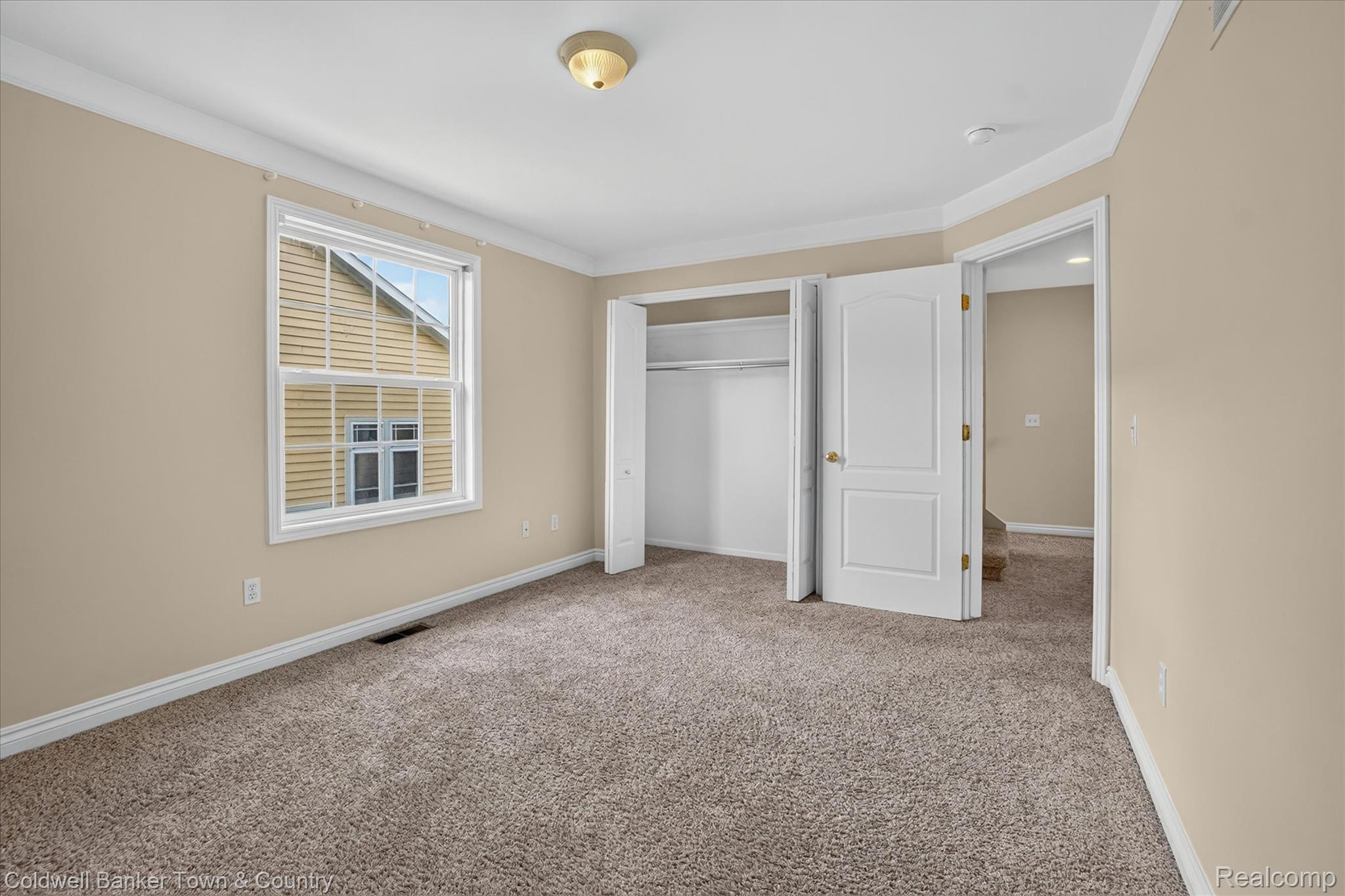 1725 Town Commons Drive Howell, MI 48855 - Photo 36 of 53 Carpeted room featuring a double-hung window, crown molding, a built-in closet with double bifold doors, and a ceiling-mounted light fixture