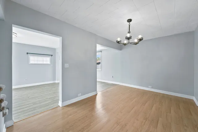 an empty room with wooden floor chandelier and windows