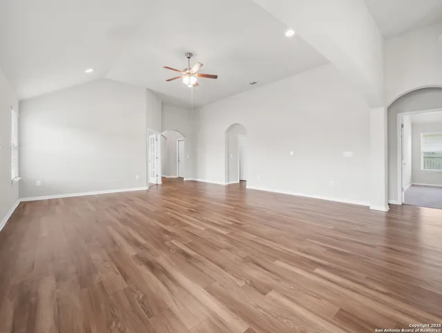 a view of an empty room with wooden floor and a ceiling fan
