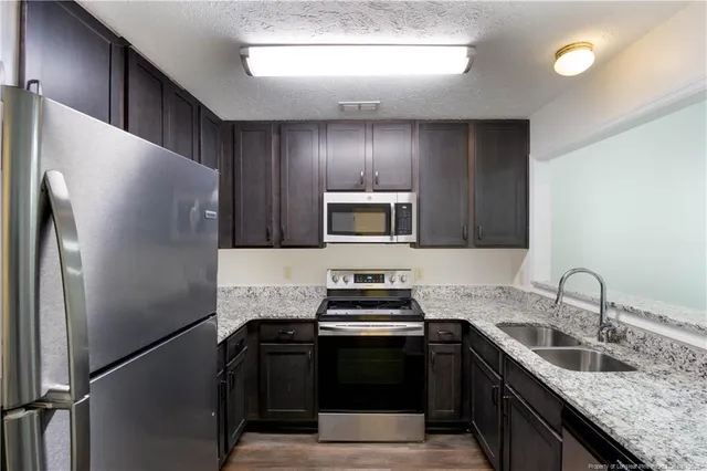 a kitchen with granite countertop stainless steel appliances a sink cabinets and a stove