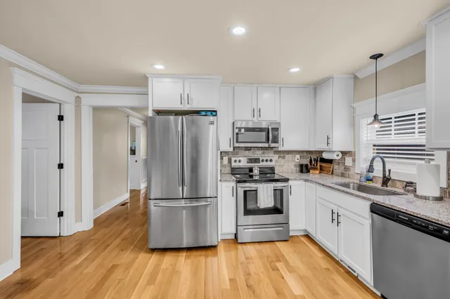 a kitchen with a refrigerator a sink dishwasher a stove and white cabinets with wooden floor