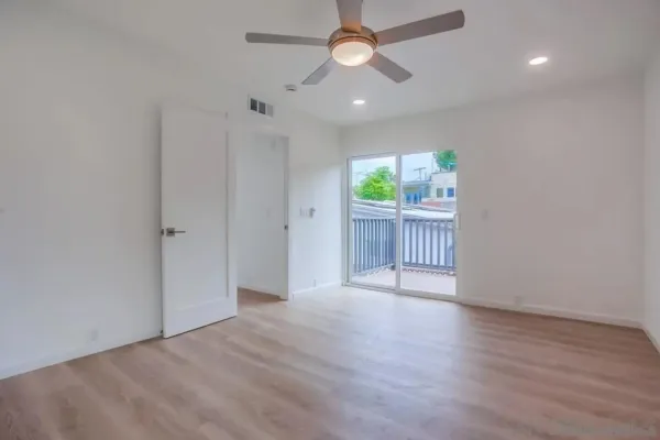 an empty room with wooden floor chandelier fan and windows