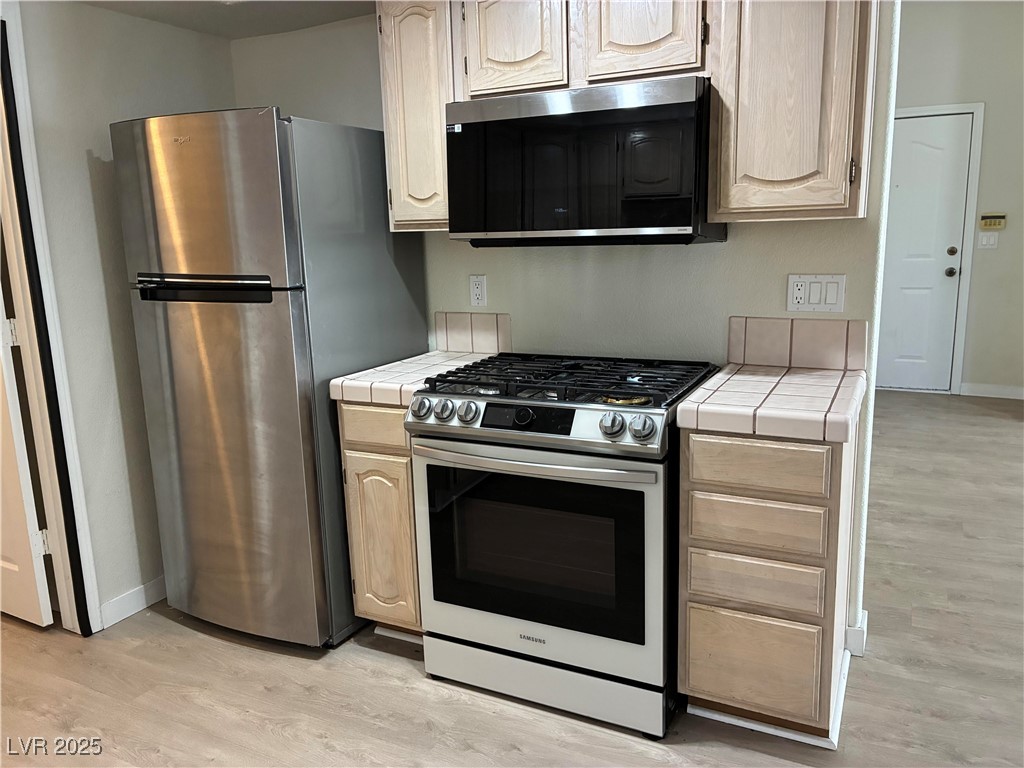 701 Capri Drive, Unit 5C Boulder City, NV 89005 - Photo 4 of 8 Kitchen featuring appliances with stainless steel finishes, tile countertops, light brown cabinets, and light wood-style flooring