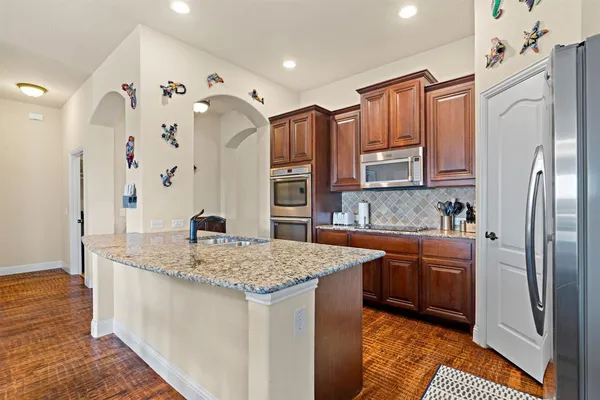 a kitchen with stainless steel appliances granite countertop a refrigerator a oven and a sink with wooden floor