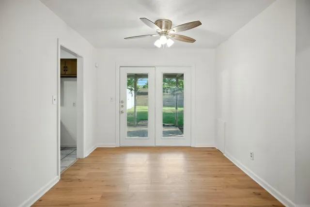 an empty room with wooden floor chandelier fan and windows