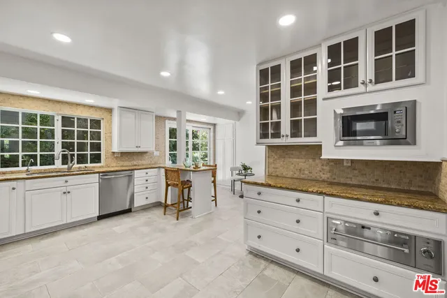a large white kitchen with granite countertop a stove a sink a window and white cabinets