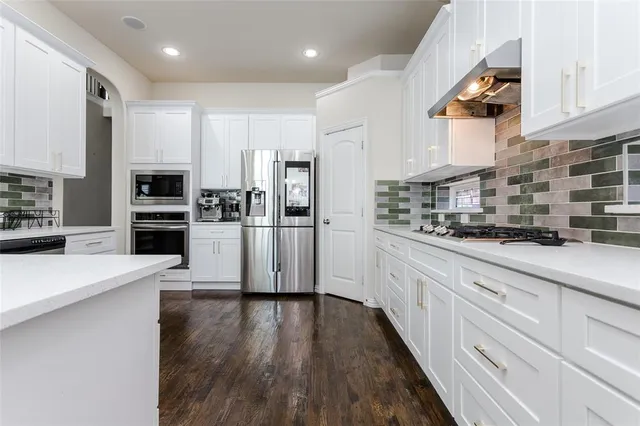 a kitchen with stainless steel appliances granite countertop a refrigerator oven a sink dishwasher and white cabinets with wooden floor