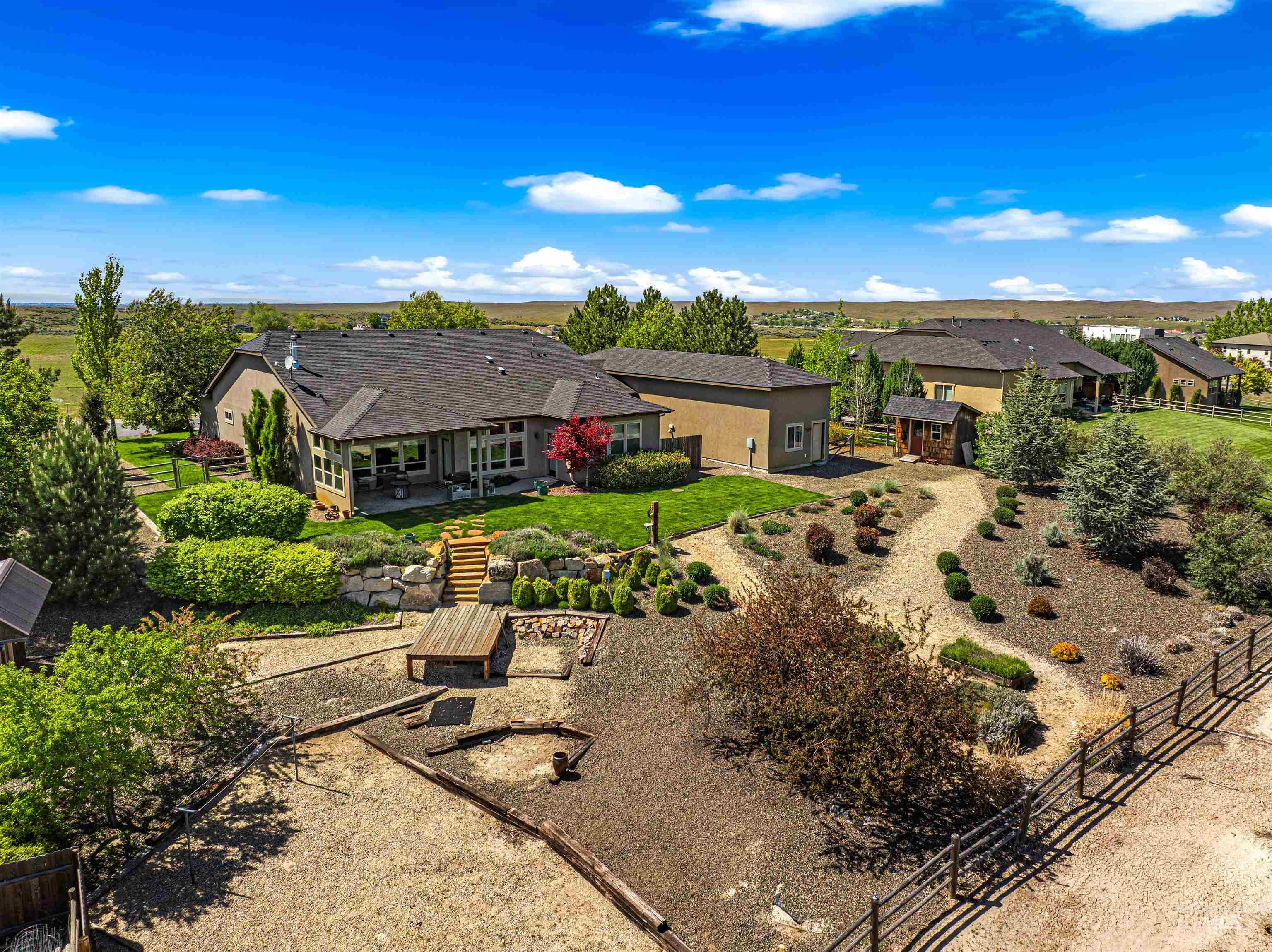 7521 North Grand Ridge Lane Eagle, ID 83616 - Photo 41 of 50 Rear exterior featuring a large patio, terraced landscaping with rock retaining walls, natural wood steps, a manicured lawn, and mature trees
