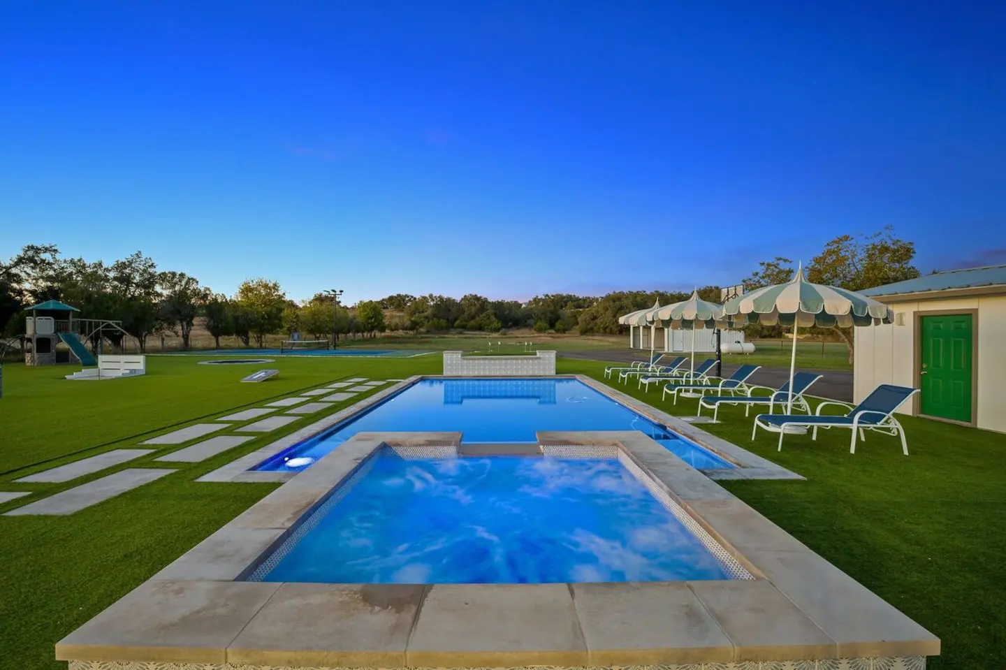 3500 Creek Road Dripping Springs, TX 78620 - Photo 3 of 21 View of pool featuring a lawn, a playground, a patio, a pool with connected hot tub, and view of scattered trees