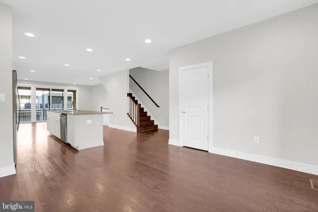 a view of an empty room with wooden floor and a kitchen