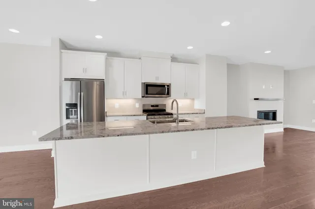 a large kitchen with granite countertop a sink a stove a microwave a refrigerator and white cabinets with wooden floor