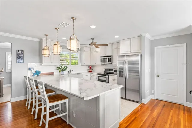 a kitchen with stainless steel appliances kitchen island granite countertop a refrigerator a stove top oven a sink dishwasher and white cabinets with wooden floor