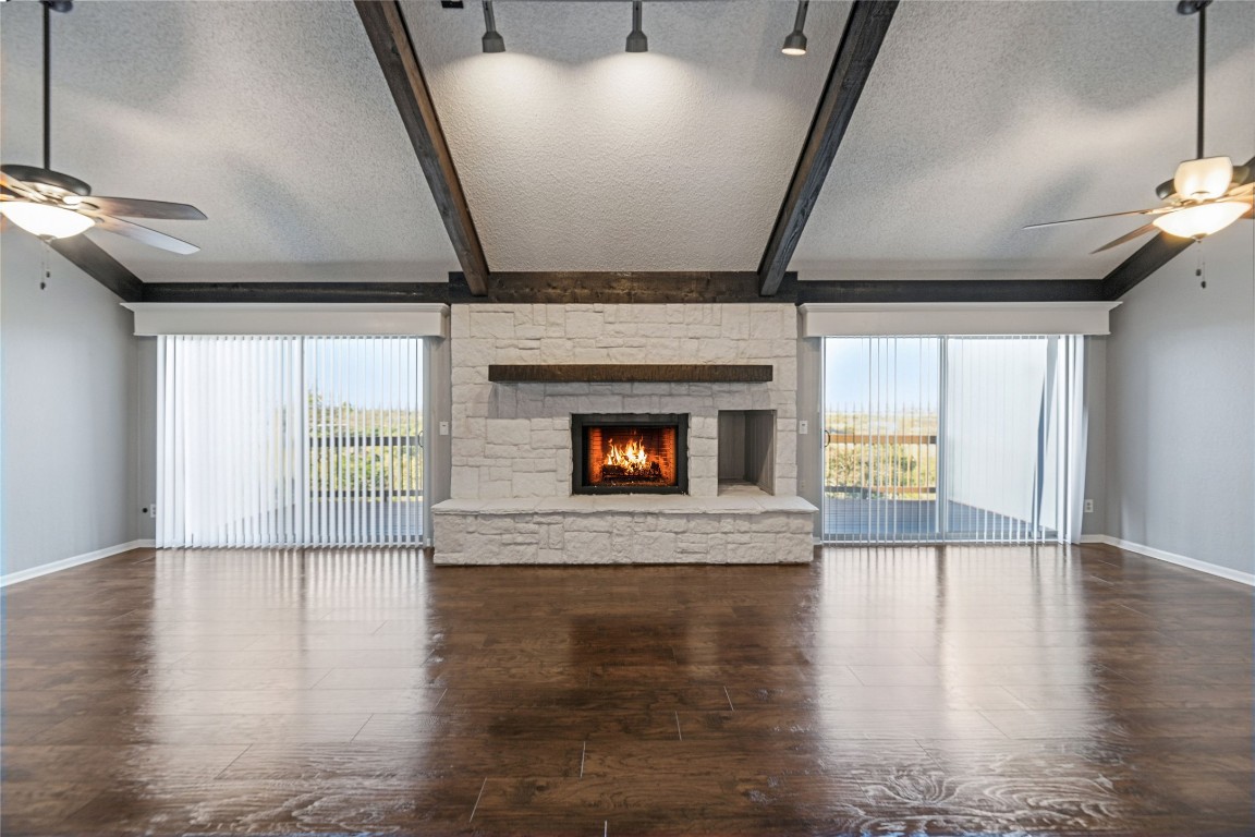 409 Hi There, Unit M Horseshoe Bay, TX 78657 - Photo 3 of 33 Unfurnished living room featuring a ceiling fan, a textured ceiling, a stone fireplace, dark wood finished floors, and beam ceiling