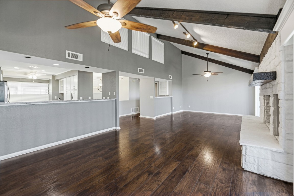 409 Hi There, Unit M Horseshoe Bay, TX 78657 - Photo 5 of 33 Unfurnished living room with a ceiling fan, dark wood finished floors, high vaulted ceiling, a stone fireplace, and beam ceiling