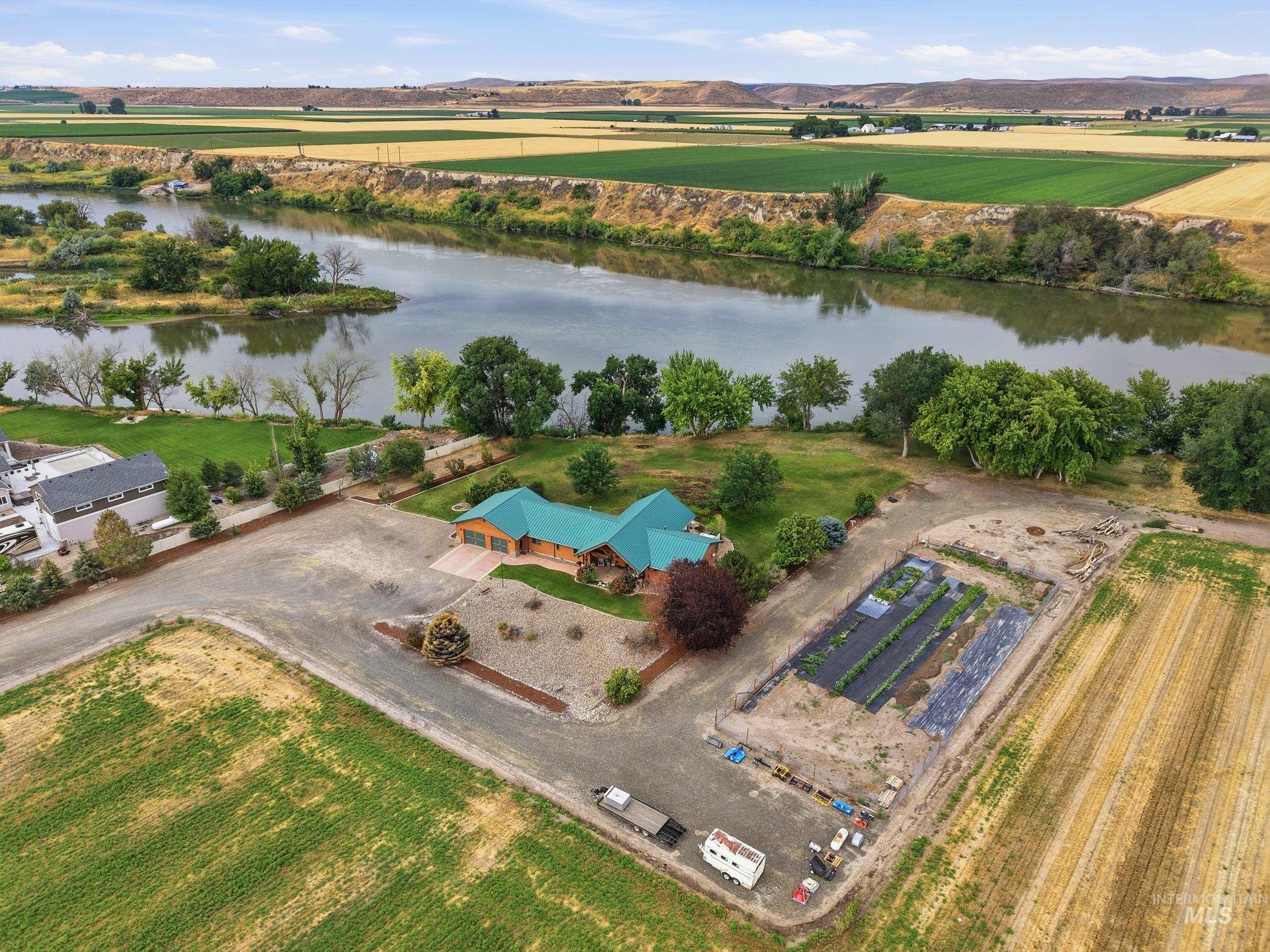 339 Airport Road Weiser, ID 83672 - Photo 38 of 49 Expansive property featuring a log-style residence with a teal roof, a large unpaved parking area, agricultural plots with planted rows, and mature trees