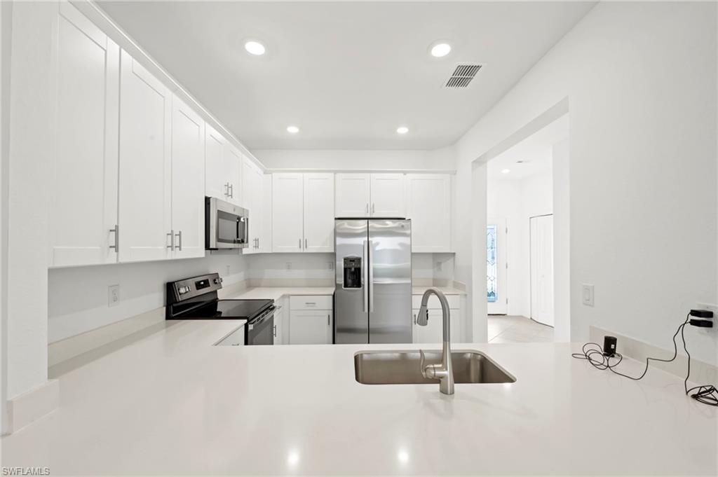 2827 Blossom Way Naples, FL 34120 - Photo 8 of 34 Kitchen with stainless steel appliances, white cabinetry, recessed lighting, light stone countertops, and a peninsula