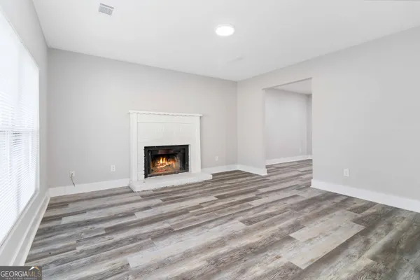 a view of an empty room with wooden floor fireplace and a window