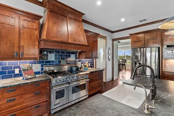 a open kitchen with stainless steel appliances granite countertop a stove a refrigerator a kitchen island a dining table and chairs with wooden floor
