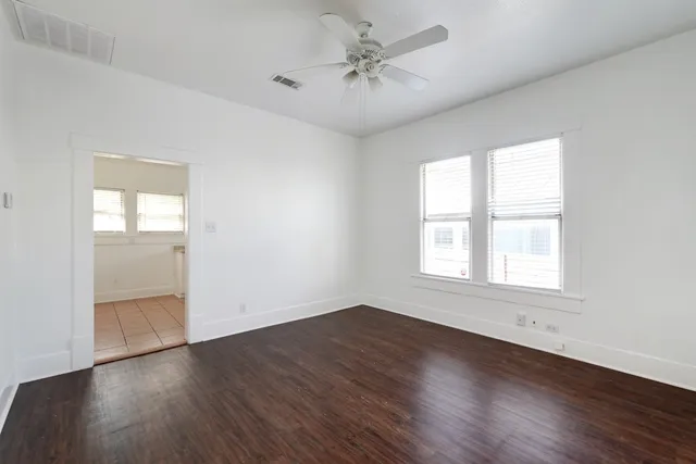 an empty room with wooden floor chandelier fan and windows