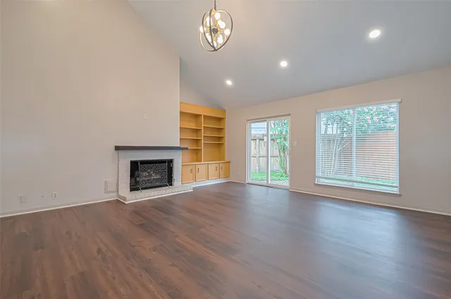 an empty room with wooden floor fireplace and windows