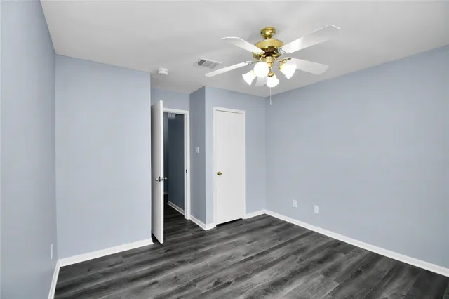 an empty room with wooden floor chandelier fan and windows