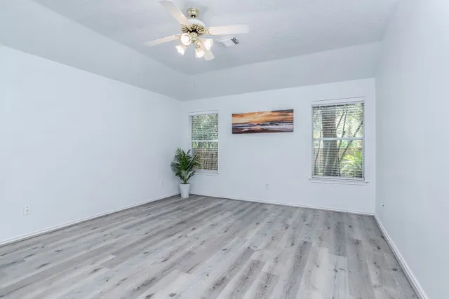 an empty room with wooden floor chandelier fan and windows