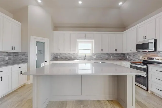 a kitchen with kitchen island granite countertop a stove a sink and white cabinets