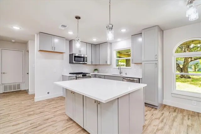 a kitchen with kitchen island a stove a refrigerator a sink a center island and wooden floor