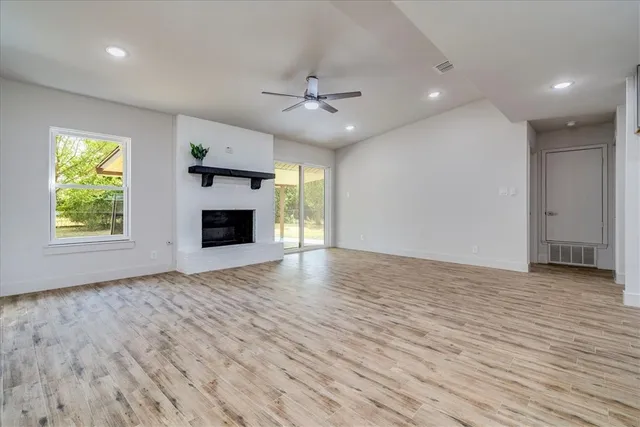 an empty room with wooden floor fireplace and windows