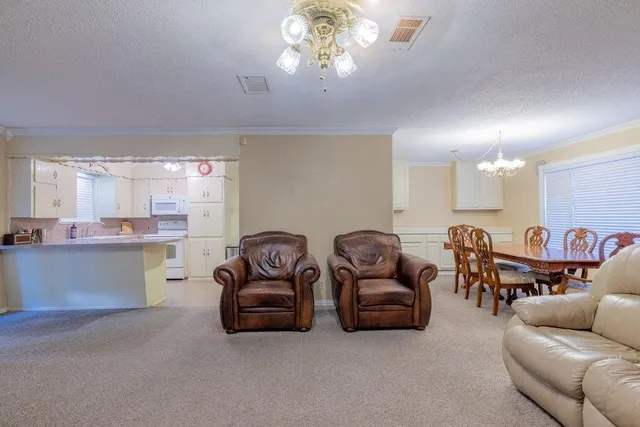 a living room with furniture a chandelier and kitchen view
