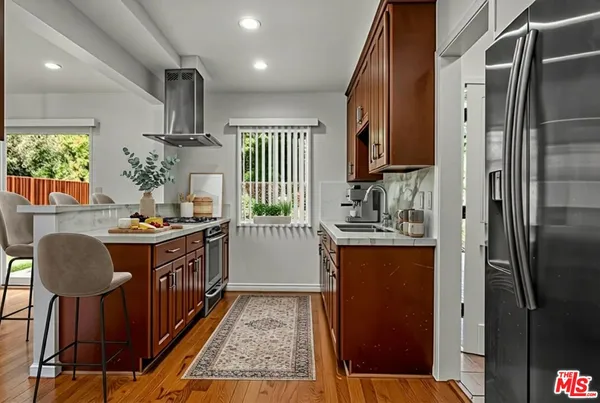 a kitchen with stainless steel appliances granite countertop a refrigerator a sink dishwasher a stove and a dining table with wooden floor