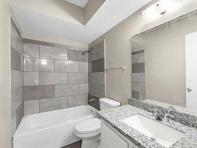 a bathroom with a granite countertop bathtub shower sink mirror and toilet
