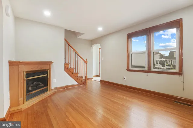 a view of an empty room with wooden floor fireplace and a window