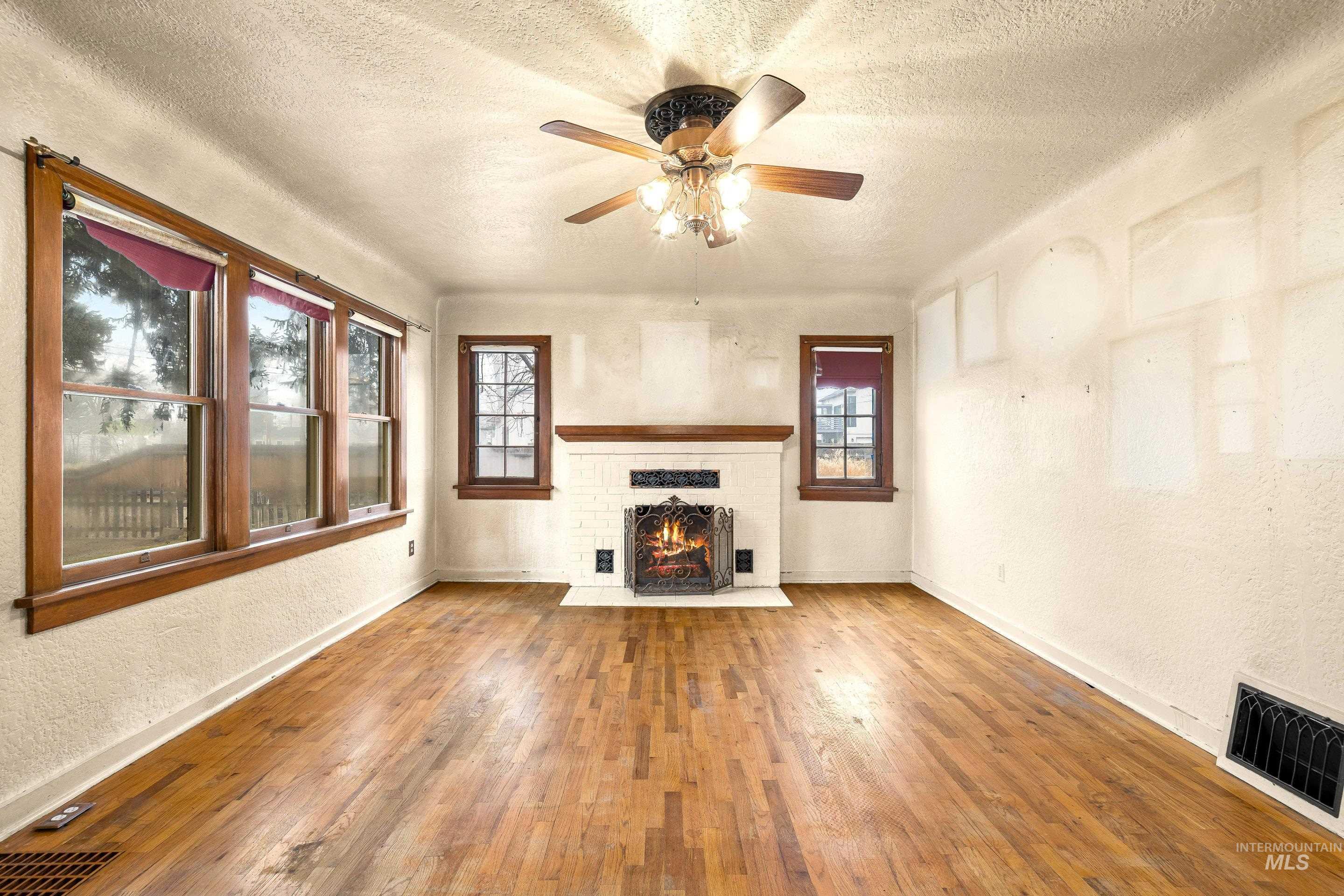 2305 South Gekeler Lane Boise, ID 83706 - Photo 6 of 33 Unfurnished living room featuring a textured wall, a brick fireplace, a textured ceiling, hardwood / wood-style flooring, and ceiling fan