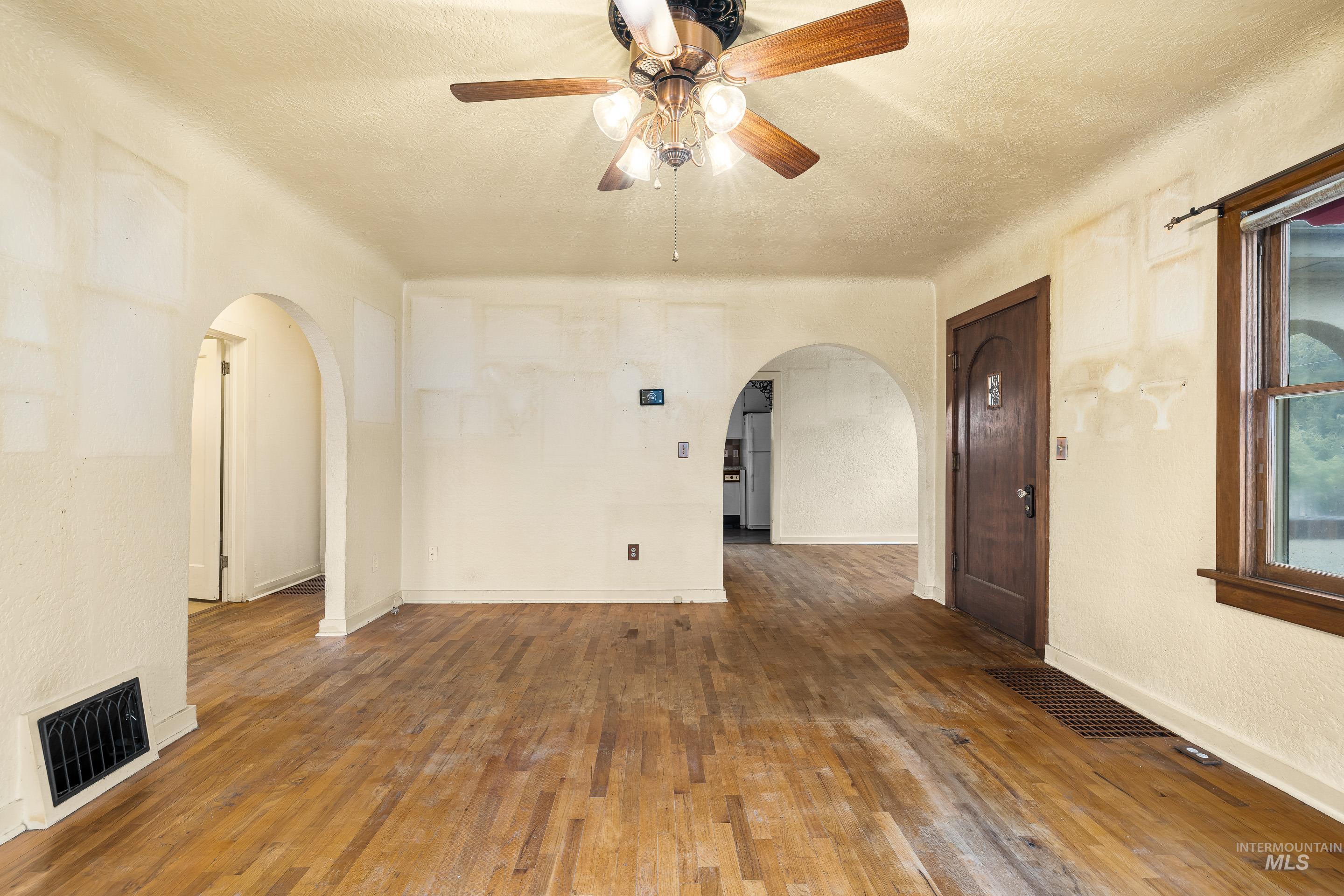 2305 South Gekeler Lane Boise, ID 83706 - Photo 8 of 33 Unfurnished living room featuring wood-type flooring, arched walkways, a textured ceiling, ceiling fan, and a textured wall