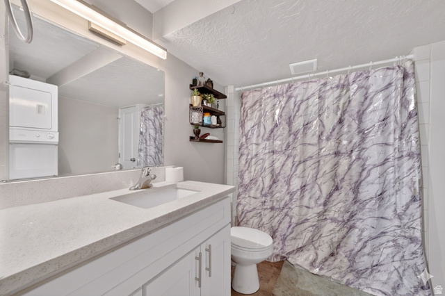 7879 Oak Street Midvale, UT 84047 - Photo 22 of 32 Bathroom featuring a single vanity with a light-toned countertop, an integrated sink, a large wall-mounted mirror, and a stacked washer and dryer unit