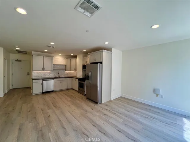 a view of kitchen with stainless steel appliances refrigerator oven and white cabinets with wooden floor